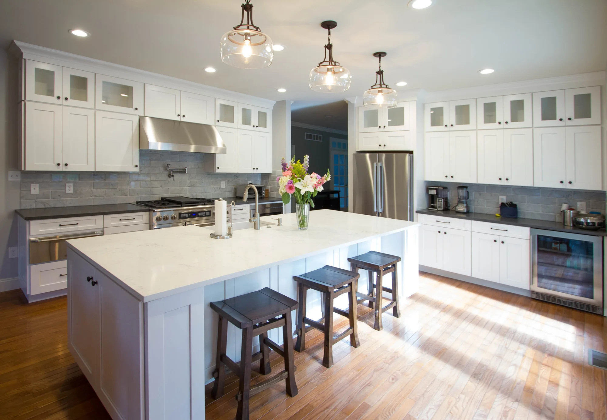 Bright white shaker kitchen remodel with a large island and pendant lighting by dRemodeling