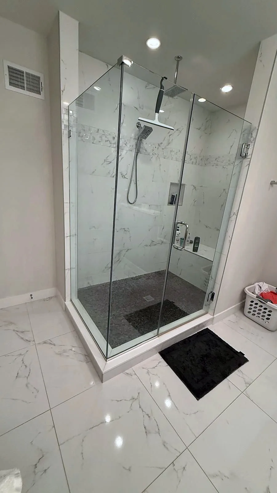Bathroom before remodel with enclosed shower and white marble-look tile.