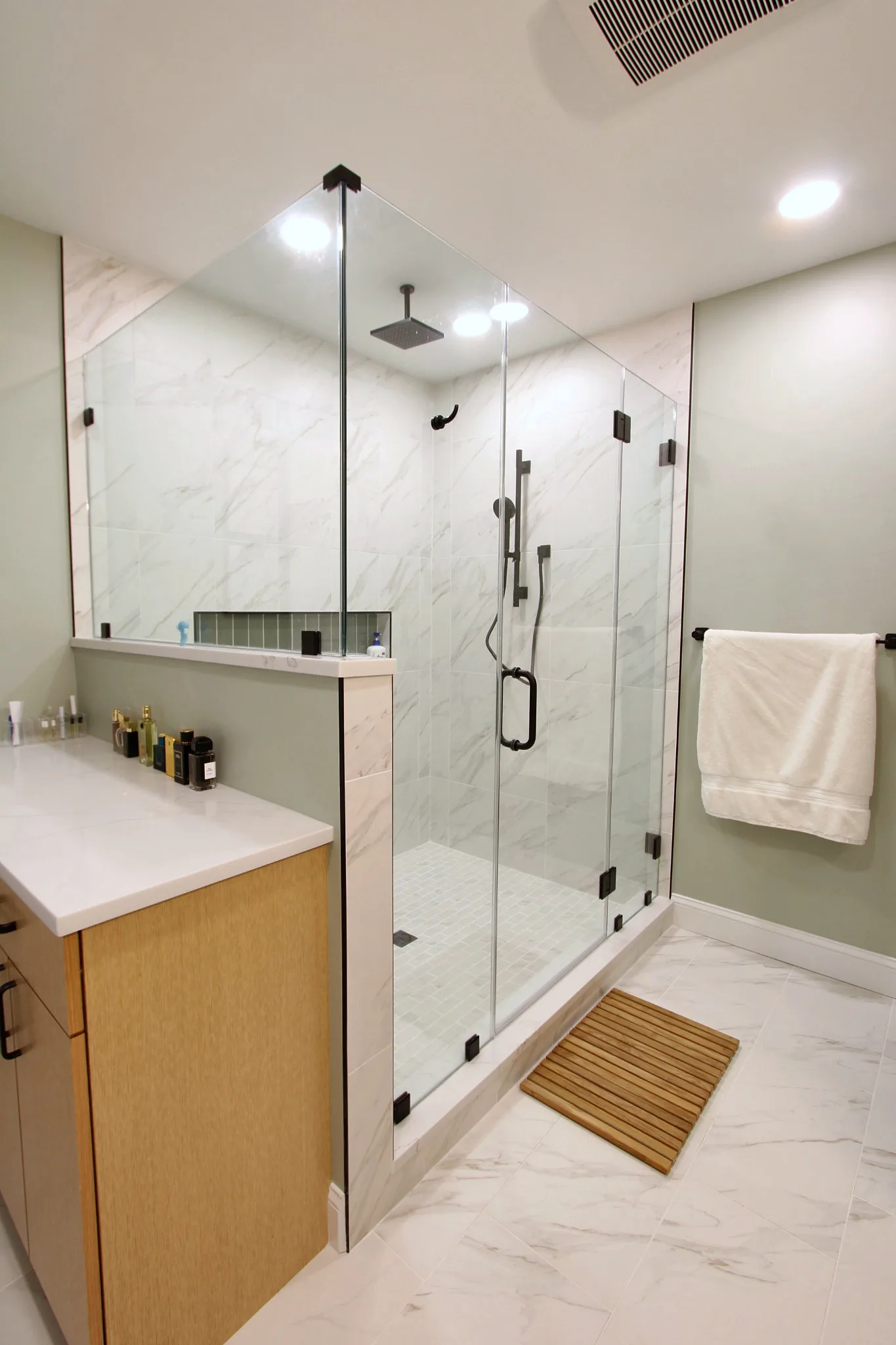 Primary bathroom after remodel with natural wood vanity and glass shower.
