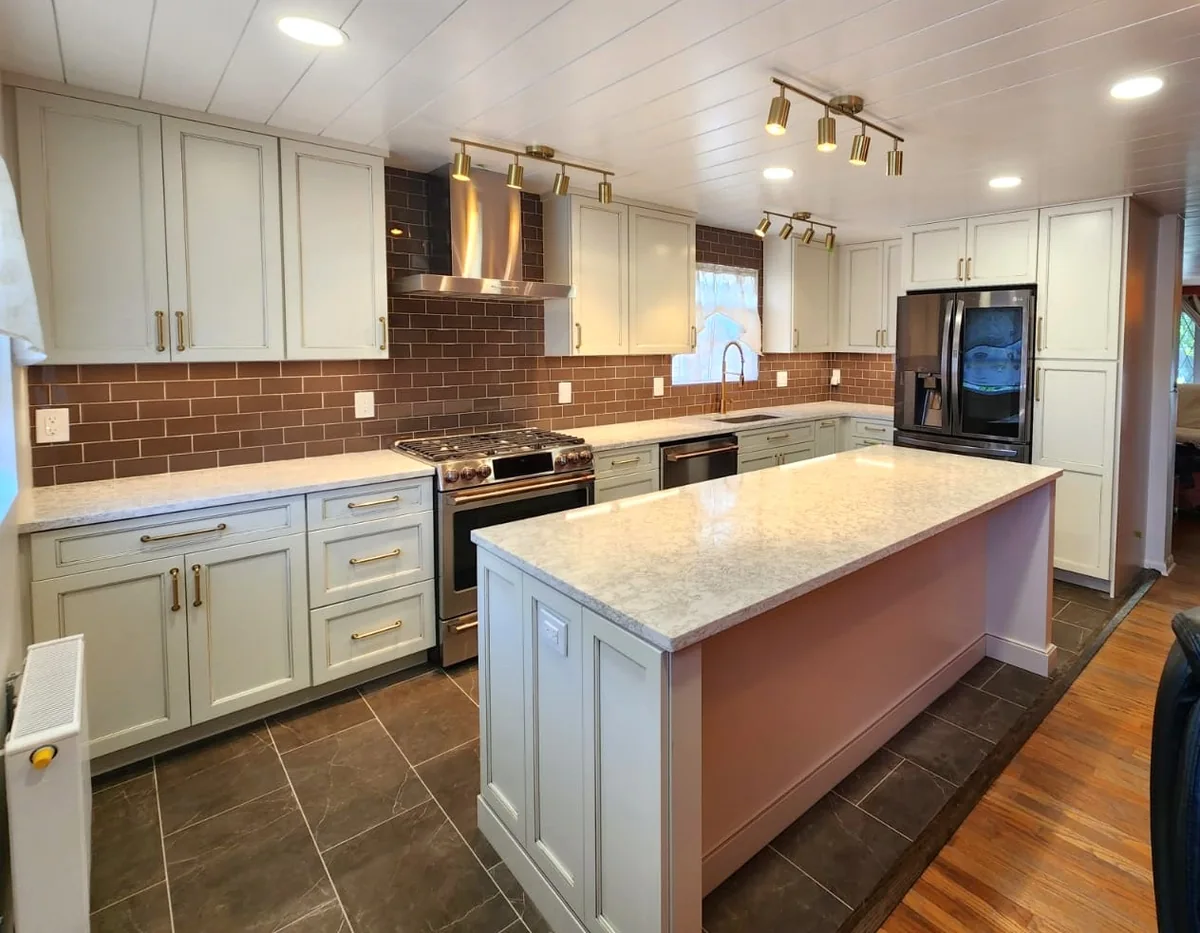 Kitchen with recessed ceiling lights, brass track lighting, white cabinets and a central island.