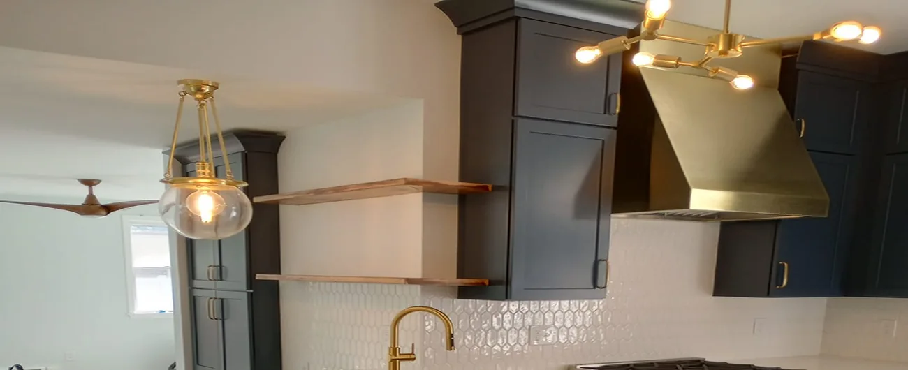 Brass pendant and branching ceiling lights with dark kitchen cabinets and open wood shelves.